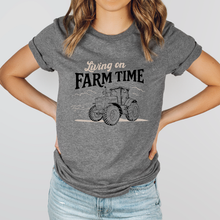 Load image into Gallery viewer, Person wearing a gray t-shirt with a tractor graphic and 'Living on Farm Time' text.