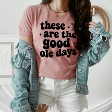 Load image into Gallery viewer, Person wearing a pink t-shirt with 'these are the good ole days' text, denim jacket, and white shorts.