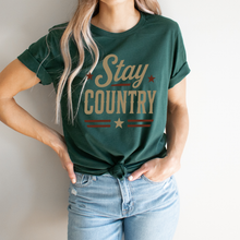 Load image into Gallery viewer, Person wearing a green t-shirt with 'Stay Country' text and stars, standing against a plain background.