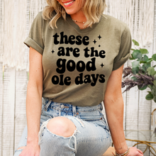 Load image into Gallery viewer, Person wearing a green t-shirt with 'these are the good ole days' text, sitting outdoors.