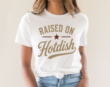 Load image into Gallery viewer, Person wearing a white t-shirt with 'Raised on Hotdish' text and star graphic.