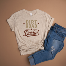 Load image into Gallery viewer, White flecked logo shirt with 'Dirt Road Darlin' text and blue jeans on a brown background