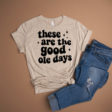 Load image into Gallery viewer, Oatmeal colored t-shirt with 'these are the good ole days' text and blue jeans on a brown background