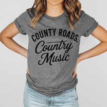 Load image into Gallery viewer, Person wearing a gray t-shirt with 'County Roads, Country Music' text on a plain background