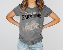Load image into Gallery viewer, Person wearing a gray t-shirt with 'Living on Farm Time' and a tractor graphic.