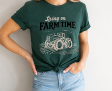Load image into Gallery viewer, Person wearing a green t-shirt with 'Living on Farm Time' and a tractor graphic.